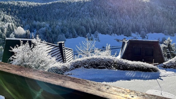 Paisaje nevado con una montaña al fondo y una cabaña de madera en primer plano.