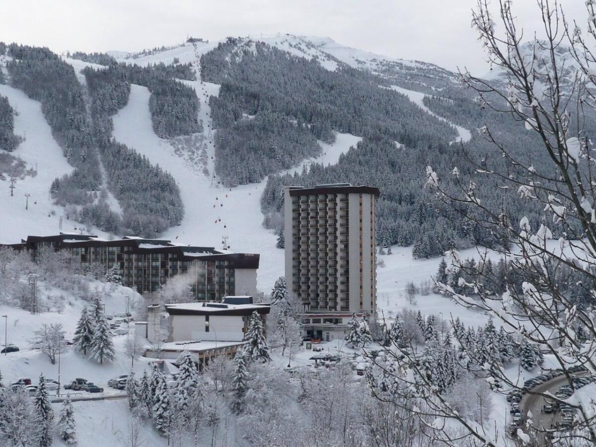 A snow-covered mountain landscape with a ski resort, including buildings and ski lifts.