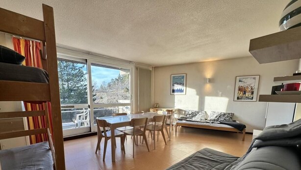 Un salón acogedor con sofá, mesa de comedor con sillas y una litera con vistas al exterior.