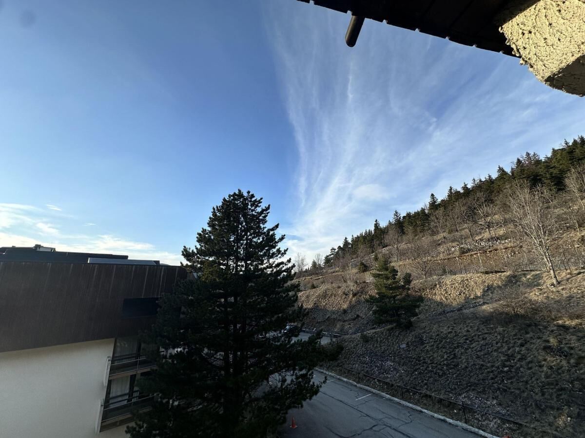 A view of a building with a clear sky and a forested hillside.