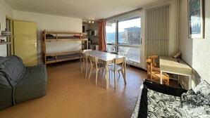 Un espacio habitable compacto con una cama litera, una mesa de comedor con sillas, un sofá y una pequeña cocina.