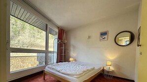 Un dormitorio con cama, ventana, escalera, mesita de noche con lámpara y espejo en la pared.
