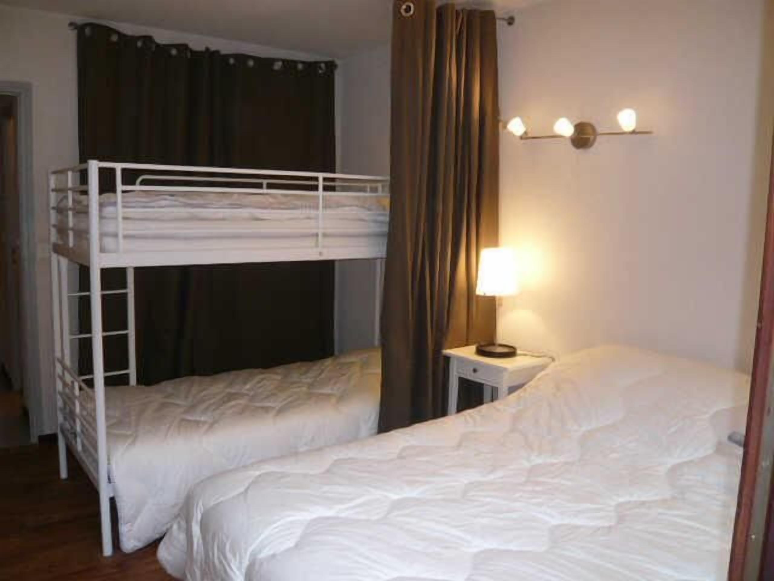 A dormitory room with two bunk beds, a bedside table with a lamp, and a curtain.