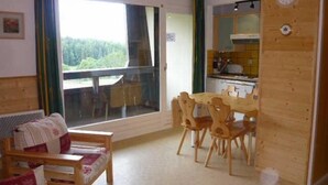Tunnelmallinen huone, jossa on puinen ruokapöytä ja -tuolit, kukkapainokuosisilla koristetyynyillä varustettu sohva ja suuri ikkuna, josta avautuu näkymä vehreään maisemaan.