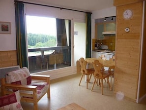 Tunnelmallinen huone, jossa on puinen ruokapöytä ja -tuolit, kukkapainokuosisilla koristetyynyillä varustettu sohva ja suuri ikkuna, josta avautuu näkymä vehreään maisemaan.