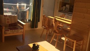 Tunnelmallinen huone, jossa on puinen pöytä, tuoleja, sohva ja näkymä metsäiselle alueelle.