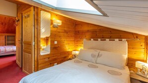 Ein gemütliches Schlafzimmer im Dachgeschoss mit holzgetäfelter Schräge, einem Bett mit weißer Bettwäsche, einem Nachttisch mit Lampe und einem Spiegel an der Wand.