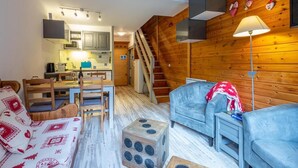 Ein gemütliches Blockhauszimmer mit Holzeinrichtung, einem Essbereich mit Tisch und Stühlen, einer Couch, einer Lampe und einer Treppe zu einer oberen Ebene.