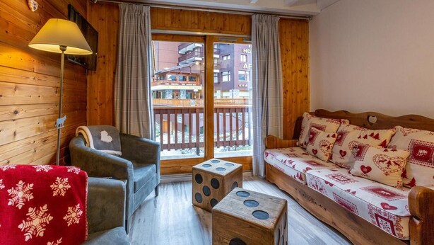 Ein gemütliches Zimmer mit Holzwänden, einer Couch mit gemusterten Kissen, einem Sessel, einem kleinen Tisch und einer Lampe.