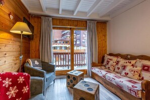 A cozy room with wooden walls, a sofa with patterned cushions, a chair, a small table, and a lamp. - 50m from ski slopes, 3rd floor, balcony, tv, 40m², Méribel-Mottaret (Méribel - Les Allues)