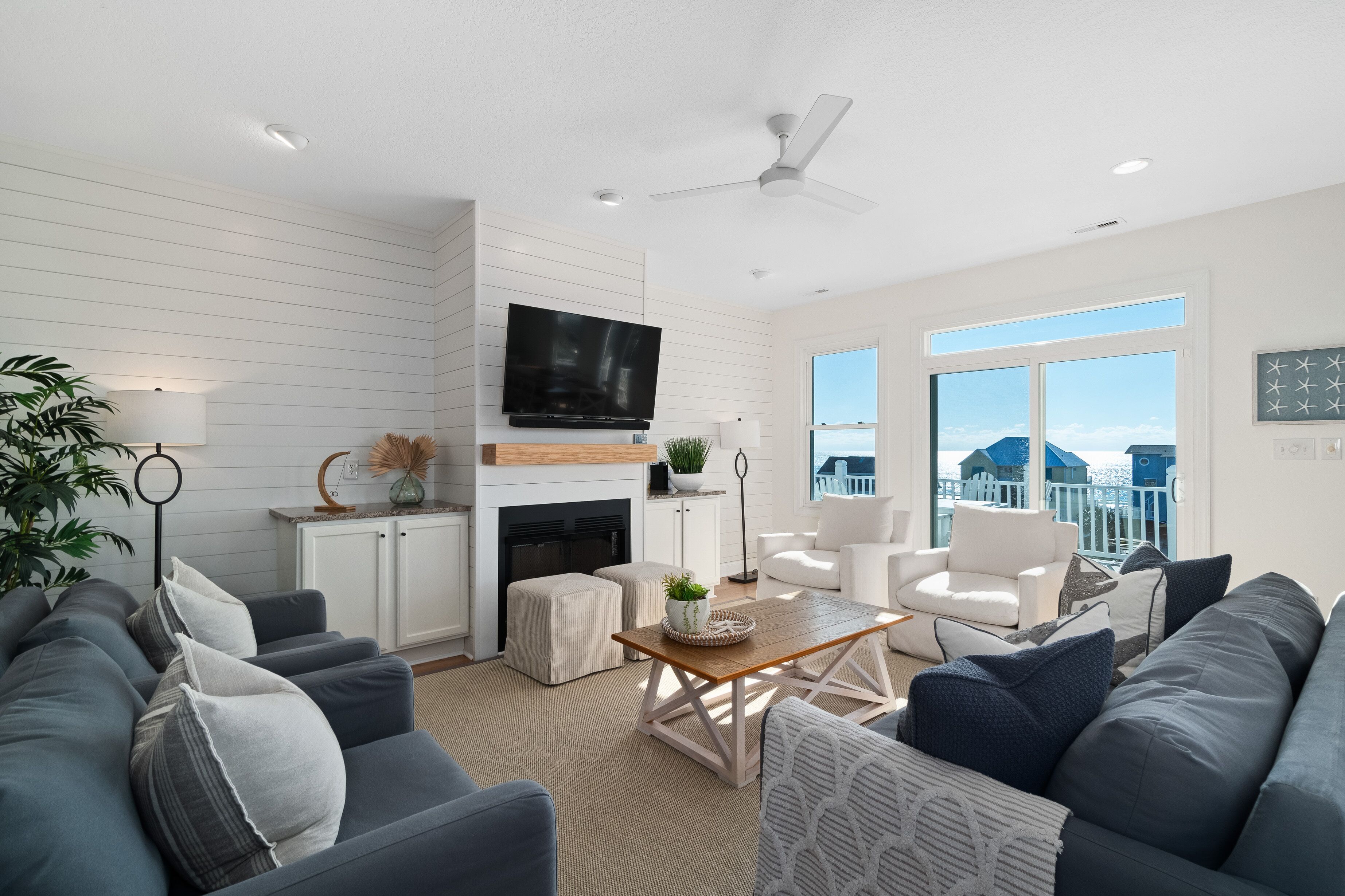 A modern living room with a fireplace, a flat-screen TV, and a large window offering a view of the ocean.