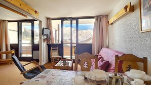 Ett rum med ett matbord dukat för te, en säng med rosa sängkläder, en tv och utsikt över bergen genom stora fönster.