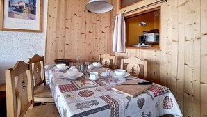 Ett rum med träpanel på väggarna, ett matbord dukat för fyra personer, en inramad tavla på väggen och ett fönster med gardiner.