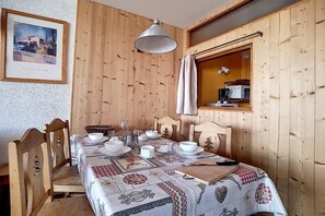 Puupaneloitu huone, jossa on neljälle katettu ruokapöytä, seinällä kehystetty taulu ja ikkunassa verhot.