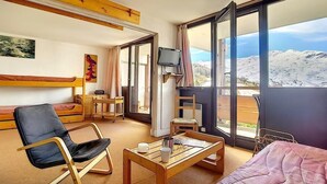Ett hotellrum med en säng, en stol, ett bord, en tv och en balkong med utsikt över bergen.