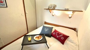 Une petite chambre accueillante, avec un lit, une table de chevet où est servi le petit-déjeuner, et une étagère avec un ours en peluche.