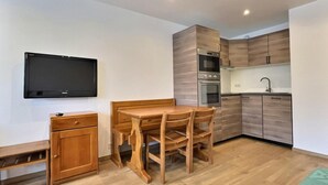 Une cuisine compacte avec des meubles en bois, un four encastré et un coin repas comprenant une table et des chaises en bois.