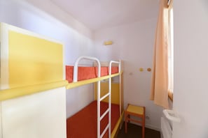 Un lit superposé avec une tête de lit jaune, une petite chaise en bois et une fenêtre avec des rideaux.