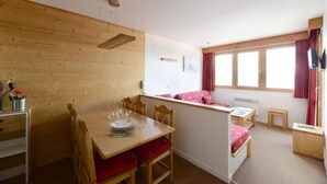A cozy room with a wooden dining table, chairs, a small kitchenette, and a window with curtains. - 100m from resort center, 5th floor, view ski slopes, balcony, tv, 39m², La Plagne (La Plagne)