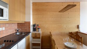 A compact kitchen with wooden cabinets, a microwave, a sink, and a dining area with a table set for four. - 100m from resort center, 5th floor, view ski slopes, balcony, tv, 39m², La Plagne (La Plagne)