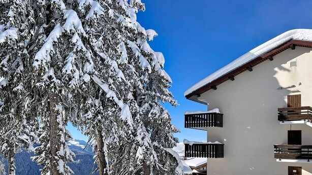 Un edificio cubierto de nieve con balcones y vistas a árboles y montañas nevadas.