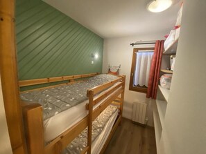 Ein Schlafraum mit Etagenbetten, einer grünen Wand, einem Heizkörper und einem Fenster mit Vorhängen.