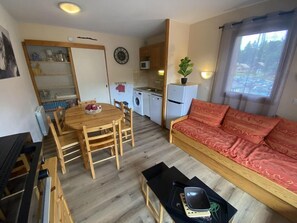 A compact living space with a dining table, chairs, a sofa, a small kitchenette, and a window with a view. - 100m from ski lifts, 2nd floor, balcony, tv, 42m², La Joue du Loup (Le Dévoluy)