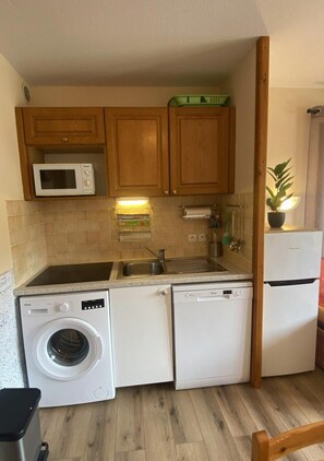 A compact kitchen with wooden cabinets, a microwave, a washing machine, and a refrigerator.