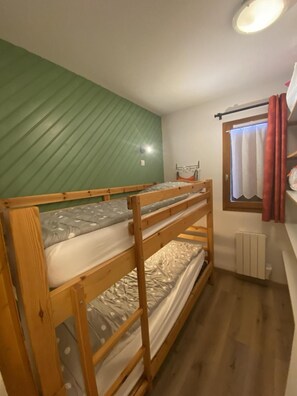 A bunk bed with a green wall behind it, a window with curtains, and a radiator on the floor.