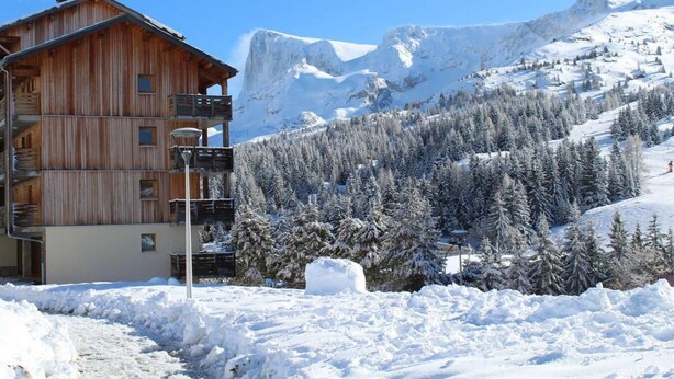 Un bâtiment en bois doté de nombreux balcons, entouré d’arbres et de montagnes couverts de neige.
