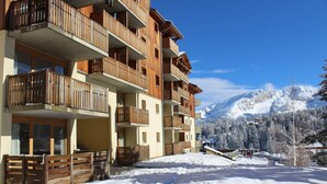 Un hôtel à plusieurs étages doté de balcons en bois, avec une piste de ski en arrière-plan et un sol recouvert de neige.