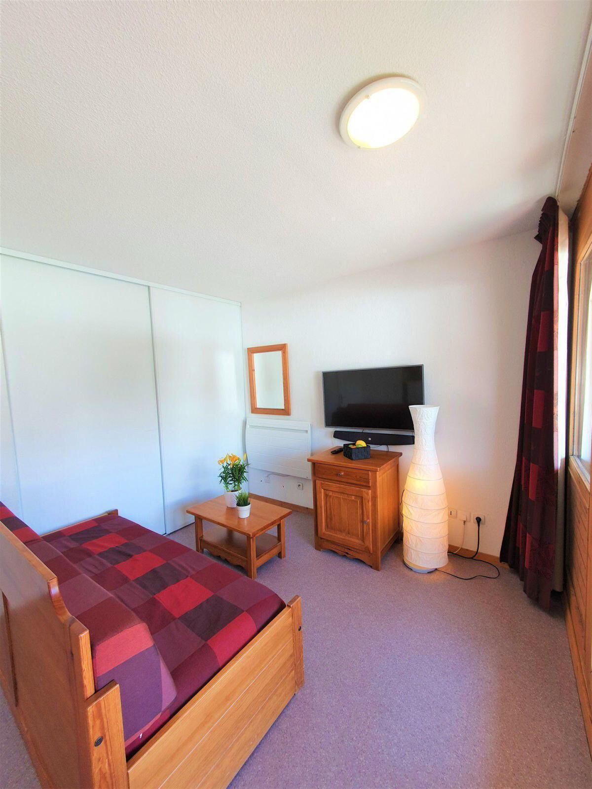 A small, tidy room with a bed, a TV, a small table with a plant, and a lamp.