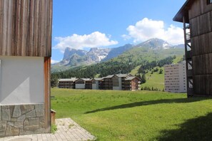 A hotel with multiple buildings, a stone wall, and a grassy field with mountains in the background. - 50m from resort center, 3rd floor, view mountain, balcony, tv, 40m², Superdévoluy (Le Dévoluy)