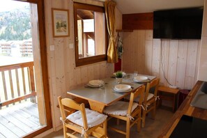Een houten eetruimte met een tafel voor vier personen, een aan de muur bevestigde televisie en een raam met uitzicht op gebouwen.