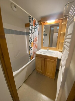 A bathroom with a bathtub, a sink, wooden cabinets, a mirror, and a shower curtain with leaf patterns.