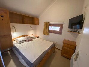 Een slaapkamer met een bed, een houten garderobe, een klein kastje, een televisie en een raam met gordijnen.