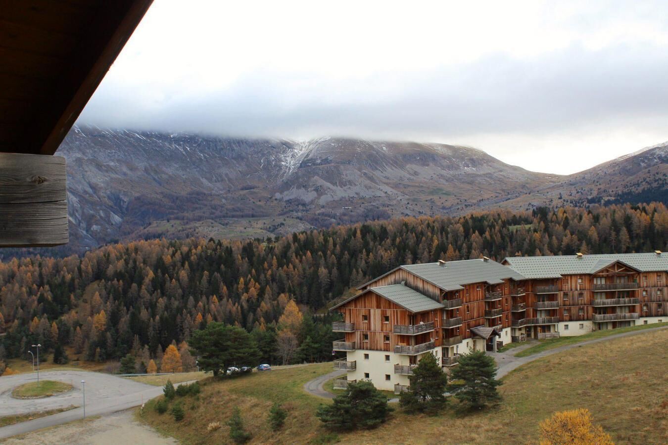 A lodge with multiple wooden buildings, a parking area, and a forested mountain backdrop.