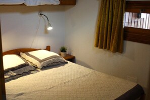 A single bed with a quilted mattress, a bedside lamp, a small potted plant, and a window with curtains.