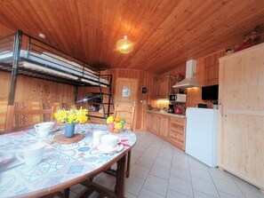 Ein Holzblockhaus-Interieur mit einem Esstisch, gedeckt für vier Personen, einer Küchenzeile mit Kühlschrank und einem Stockbett mit Leiter.