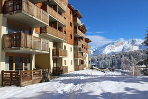 Ein mehrstöckiges Hotel mit hölzernen Balkonen, einem Skiabhang im Hintergrund und verschneitem Gelände.
