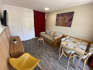 Ein gemütlicher, kompakter Wohnraum mit Sofa, Esstisch und einem kleinen Hocker.