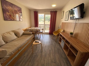 A furnished room with a sofa, a dining table, chairs, a TV, and a view through a glass door. - Ski-in/ski-out & foot of the slopes, 7th floor, view ski slopes, balcony, parking, tv, 28m² (Le Dévoluy)