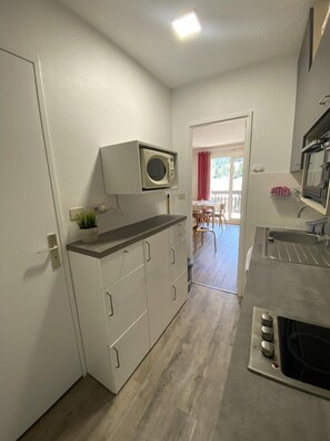 A compact kitchen with a microwave, oven, and sink. There is a dining area with a table and chairs visible through an open door. - Ski-in/ski-out & foot of the slopes, 7th floor, view ski slopes, balcony, parking, tv, 28m² (Le Dévoluy)
