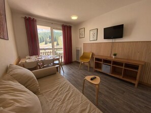 Ein Wohnzimmer mit einer Couch, einem Esstisch mit Stühlen, einem Fernseher und einer Holzkommode.