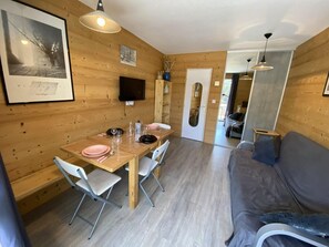 Ein Holzinnenraum mit Esstisch, Stühlen, einer Couch und einem Fernseher.