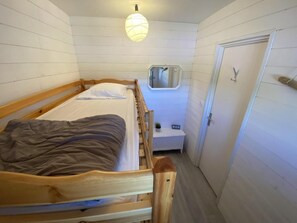 Ein kleines, schlichtes Zimmer mit einem Einzelbett, einem Nachttisch, einem Spiegel und einer Tür.