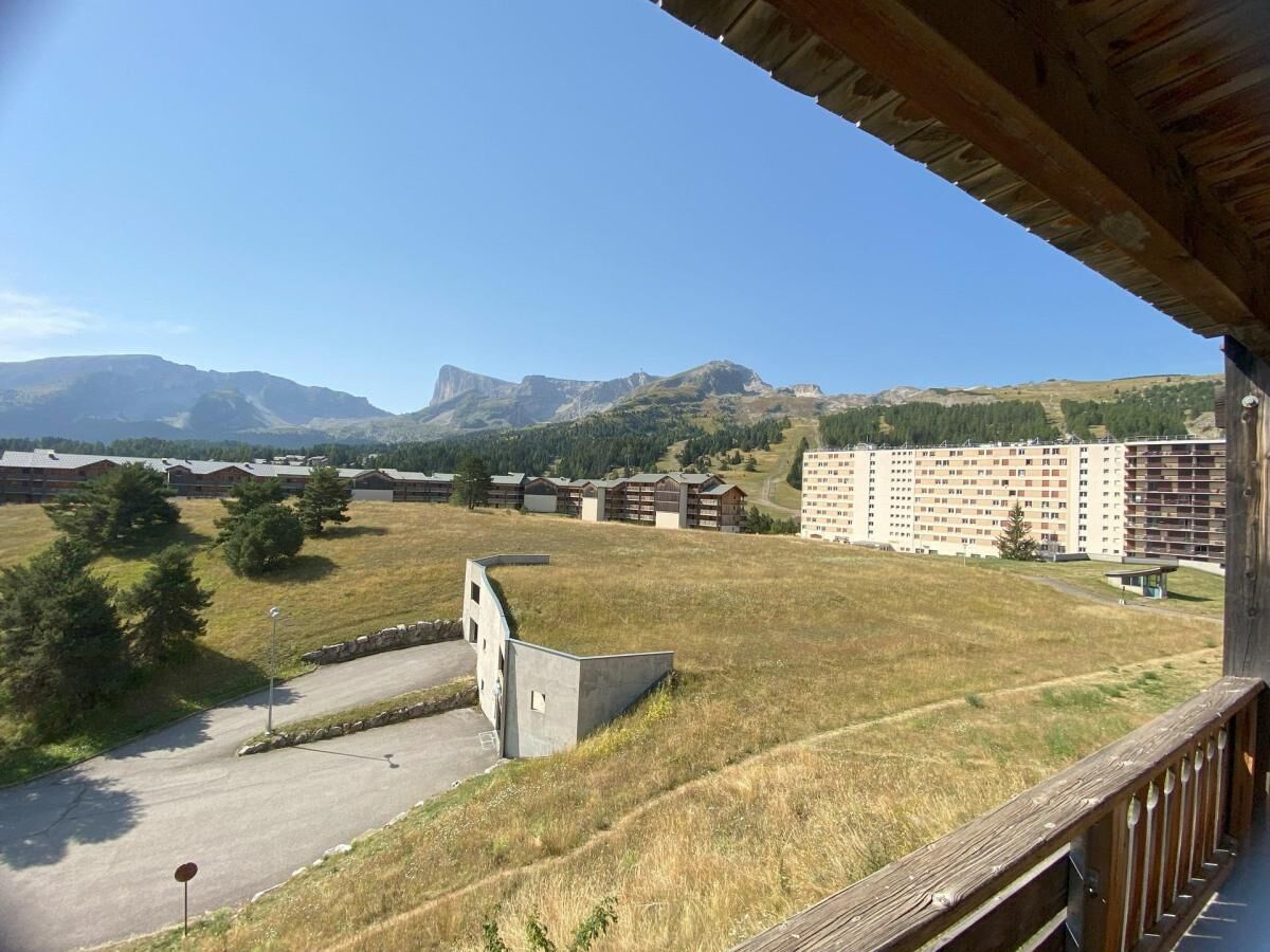 A view from a balcony overlooking a grassy field, a parking area, and a large building with multiple floors.