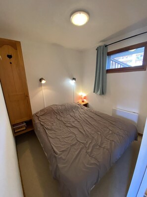 Ein Schlafzimmer mit einem Bett, einer Nachttischlampe, einer Deckenleuchte, einem Fenster mit Vorhängen und einer Heizung.