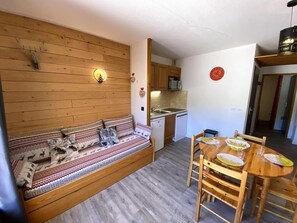 A cozy room with a wooden sofa, a dining table with chairs, a small kitchen area, and a wall-mounted clock. - 100m from ski lifts, Ground floor, terrace, tv, 28m², La Joue du Loup (Le Dévoluy)