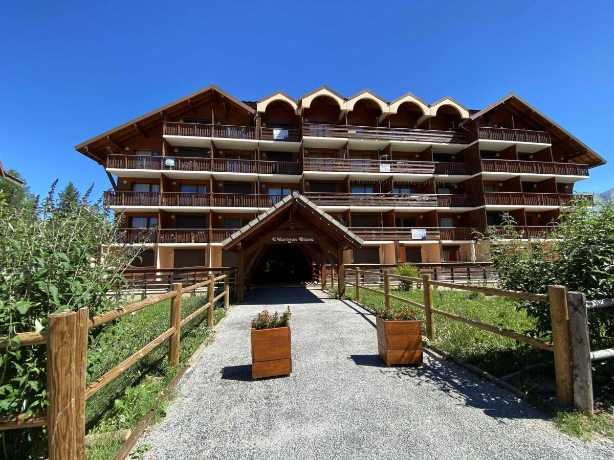 Un immeuble en bois à plusieurs étages, doté de balcons, d’une entrée centrale et d’un chemin de gravier menant à l’entrée.